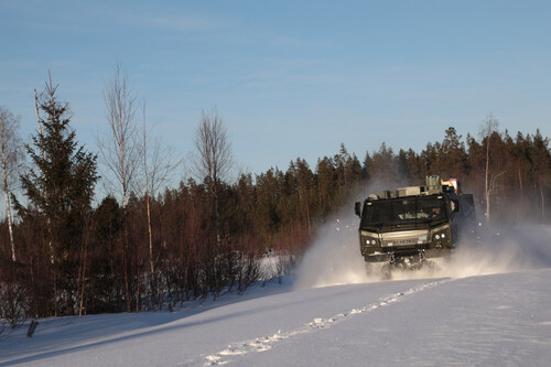 Military truck driving through snowy forest landscape with trees and clear sky