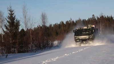 Military truck driving through snowy forest landscape with trees and clear sky