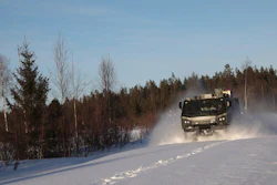 Military truck driving through snowy forest landscape with trees and clear sky