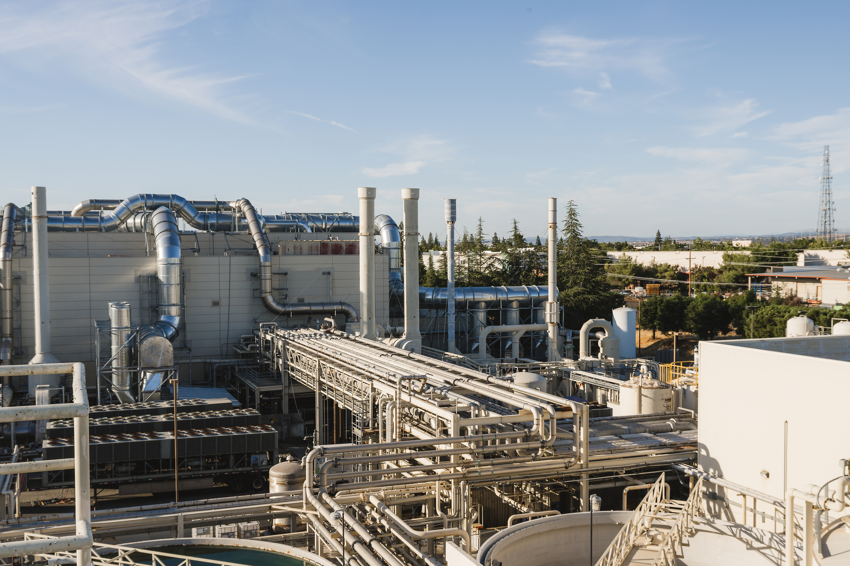 Industrial chemical processing facility with large storage tanks, interconnected piping, and manufacturing equipment under clear sky