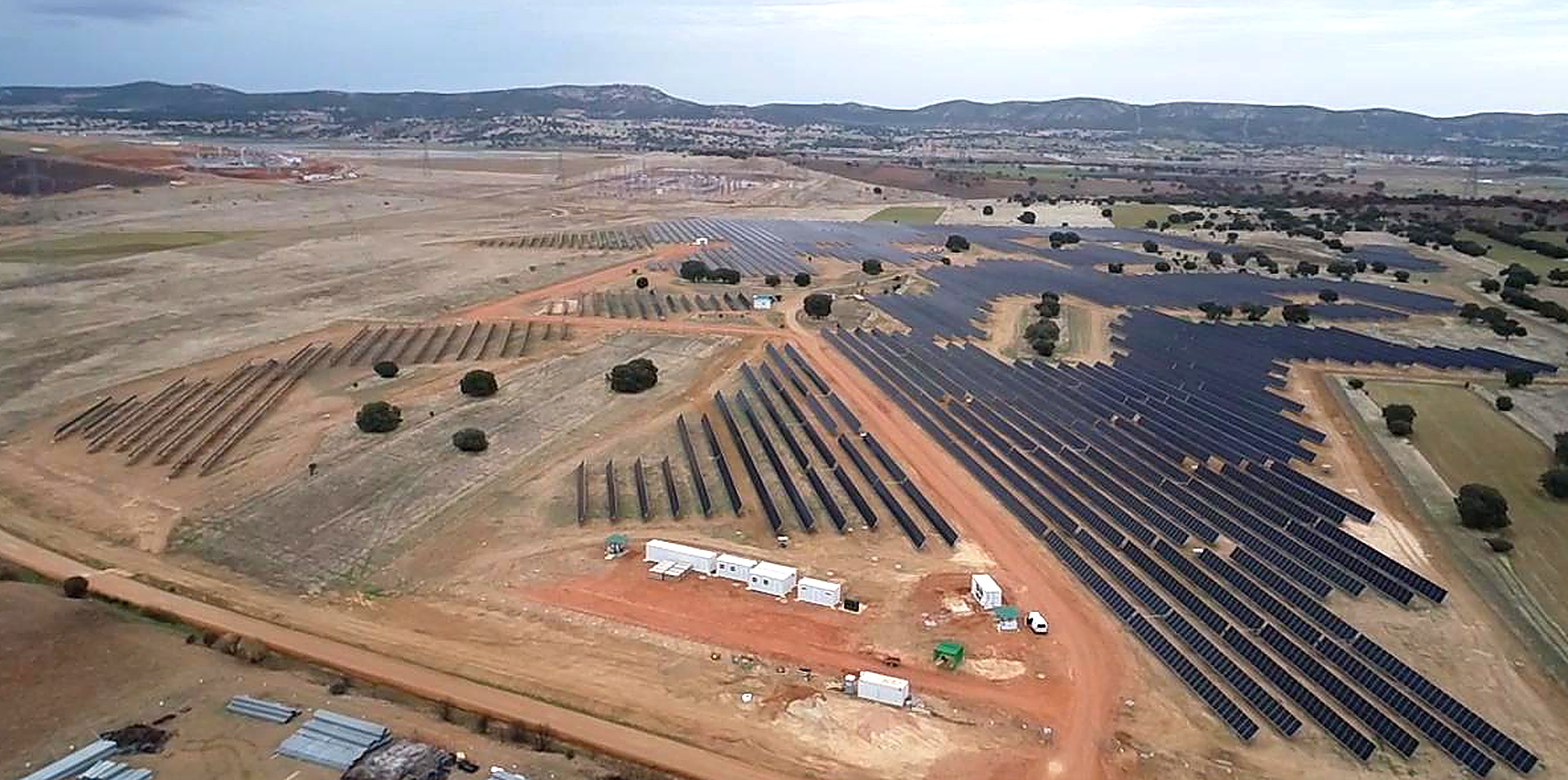 Aerial view of solar panel farm with white buildings and scattered trees in agricultural landscape