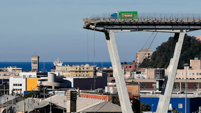 Cargo truck on elevated bridge structure above port city with Mediterranean sea and historic architecture visible