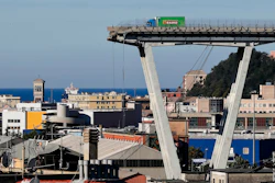 Cargo truck on elevated bridge structure above port city with Mediterranean sea and historic architecture visible