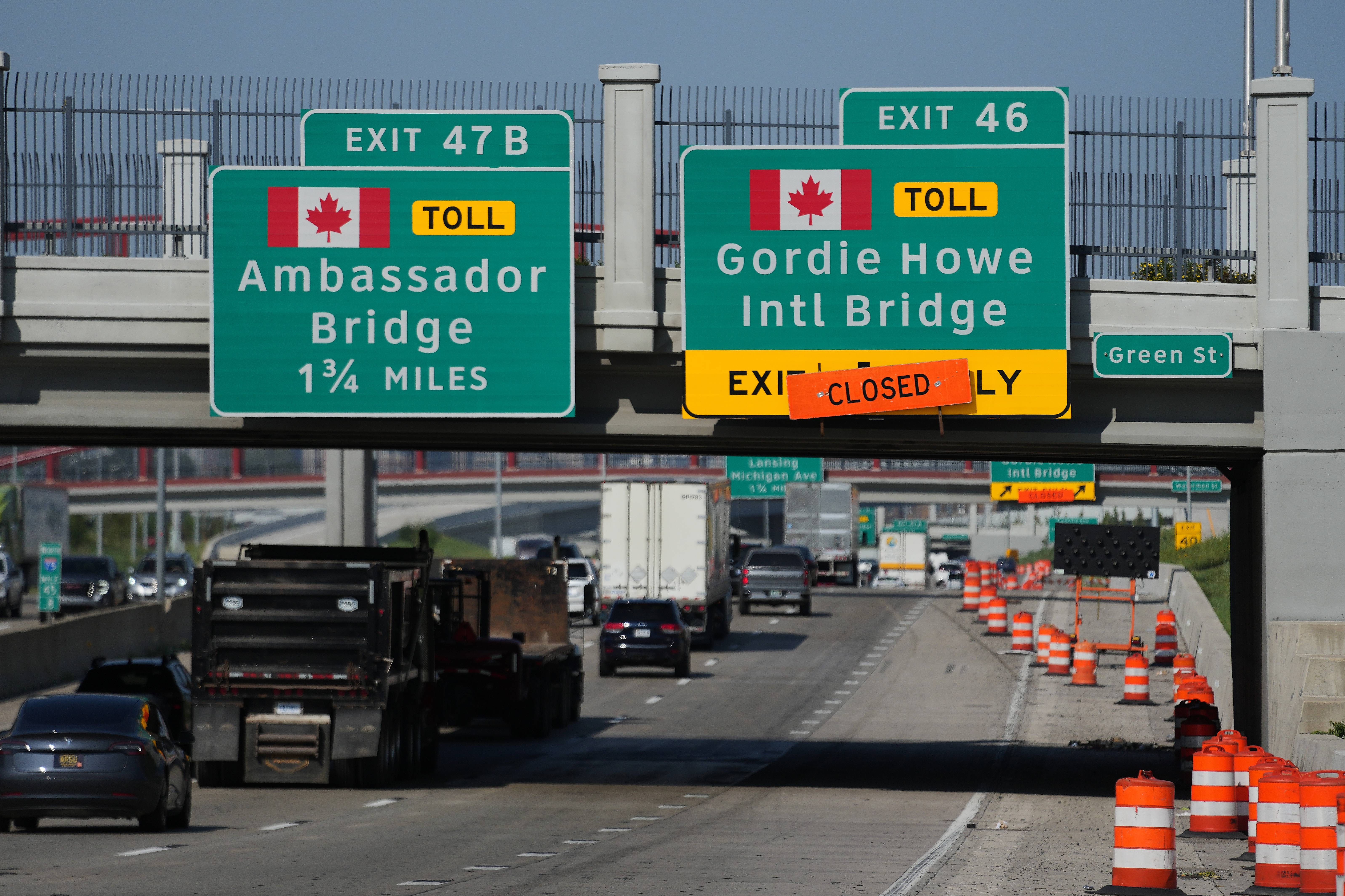 Highway exit signs for Ambassador Bridge and Gordie Howe International Bridge with construction barriers and traffic on bridge approach