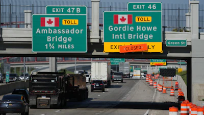 Highway exit signs for Ambassador Bridge and Gordie Howe International Bridge with construction barriers and traffic on bridge approach