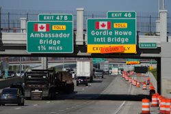 Highway exit signs for Ambassador Bridge and Gordie Howe International Bridge with construction barriers and traffic on bridge approach
