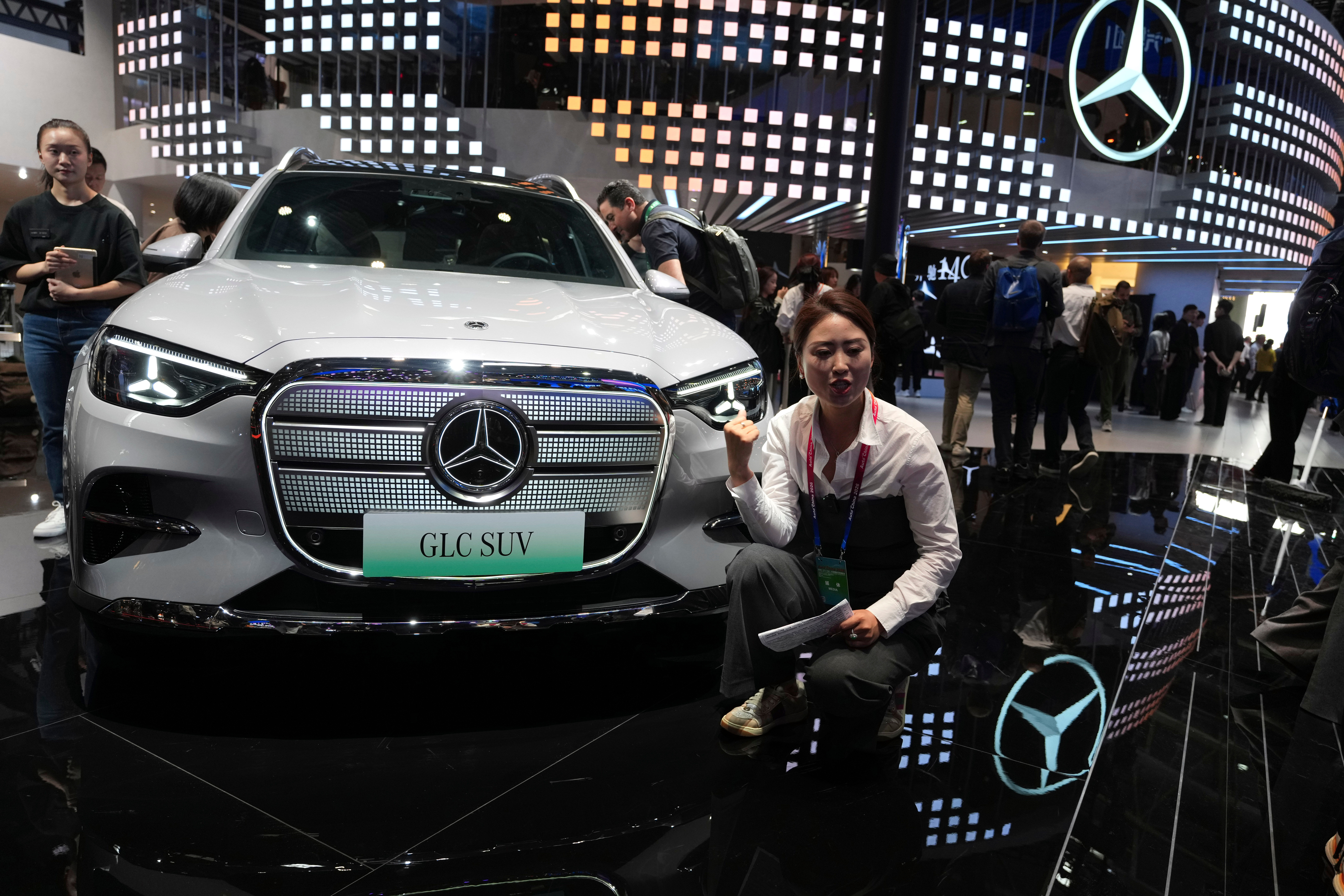 Woman posing with white Mercedes-Benz GLC SUV at auto show exhibition booth