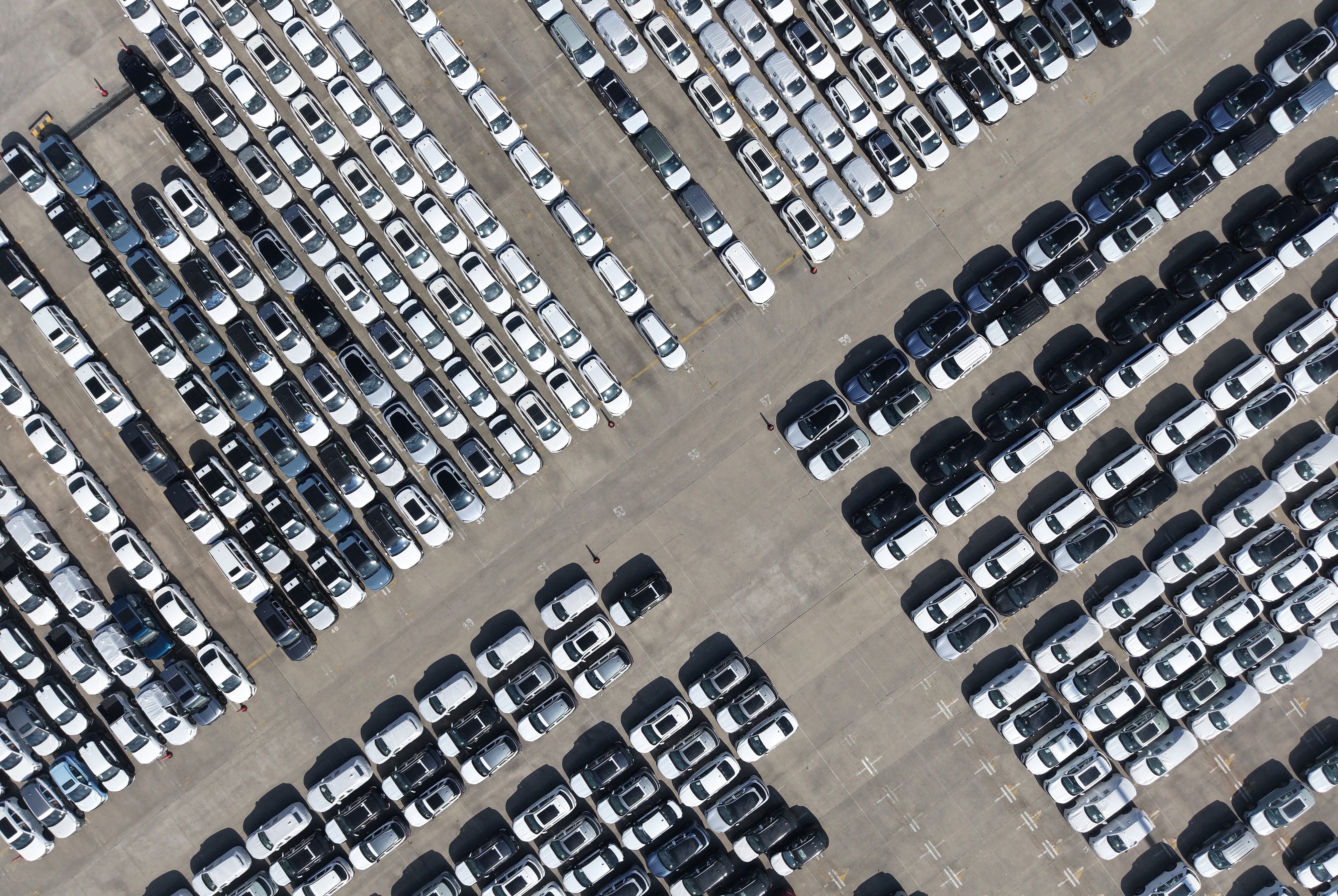 Aerial view of a large parking lot with hundreds of white and dark vehicles organized in neat rows