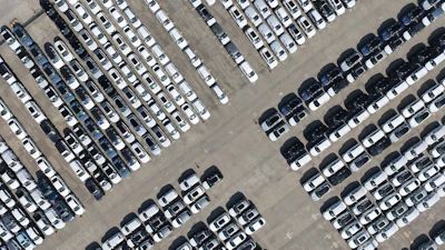Aerial view of a large parking lot with hundreds of white and dark vehicles organized in neat rows