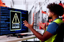 Industrial worker in safety vest gestures at computer monitor displaying 'System Hacked' warning with code in background factory setting