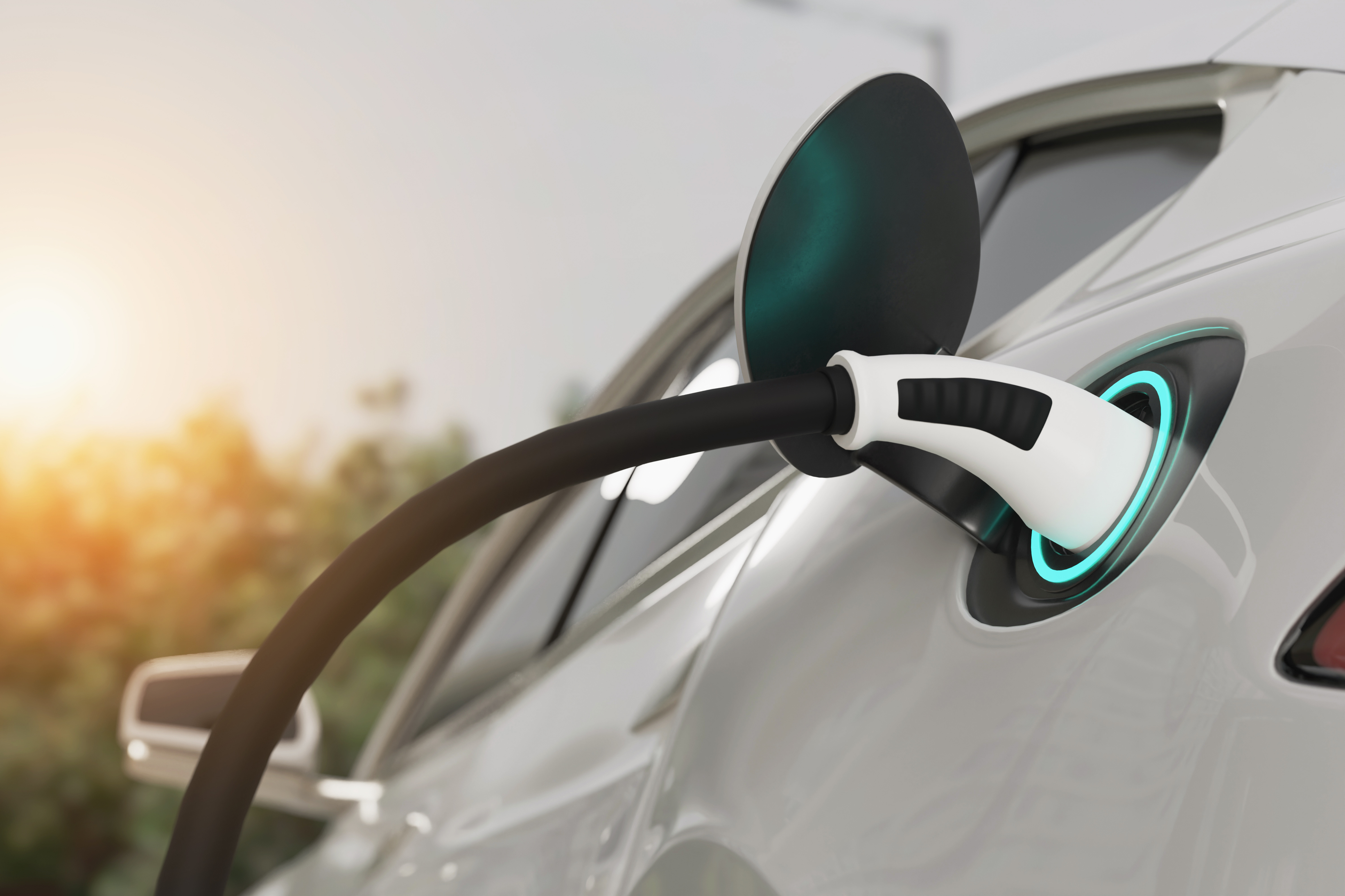 White electric vehicle charging cable connected to car with glowing cyan charging port at sunset