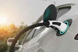 White electric vehicle charging cable connected to car with glowing cyan charging port at sunset
