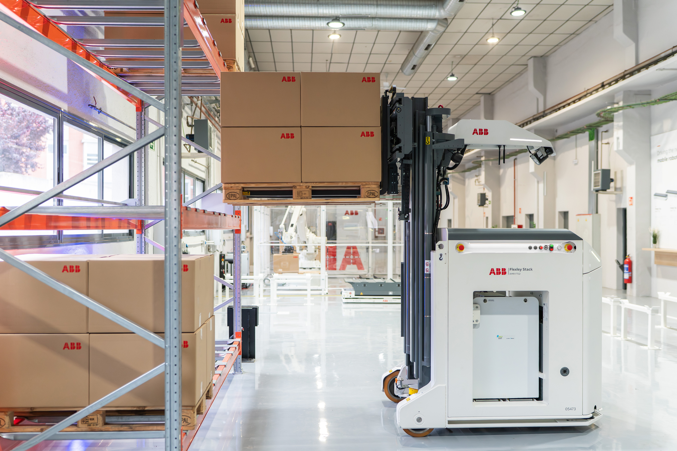 ABB warehouse facility with stacked cardboard boxes, automated robotic arm, and industrial equipment