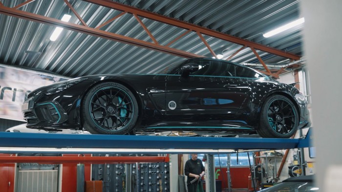 Black high-performance sports car on hydraulic lift in professional automotive workshop with industrial ceiling