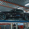 Black high-performance sports car on hydraulic lift in professional automotive workshop with industrial ceiling