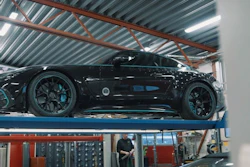 Black high-performance sports car on hydraulic lift in professional automotive workshop with industrial ceiling