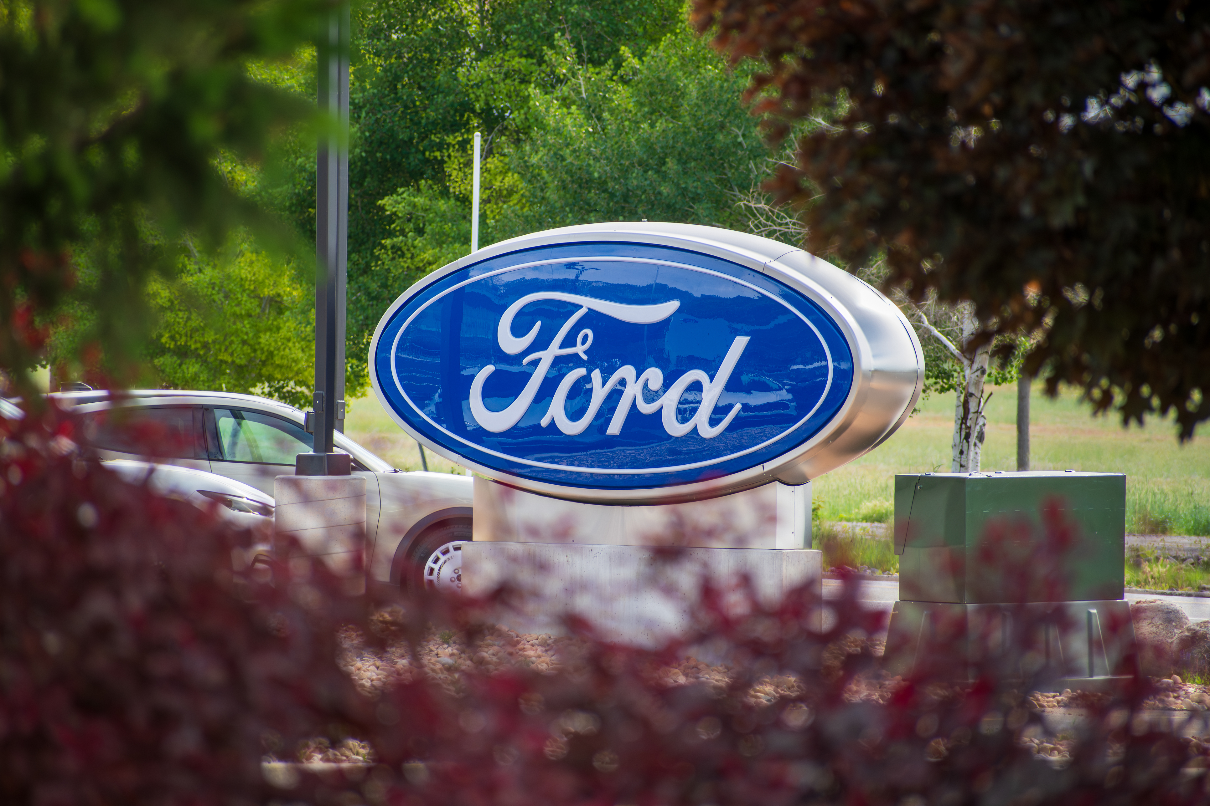 Ford logo sign mounted on pedestal surrounded by green trees and landscaping