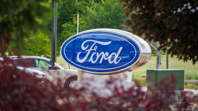 Ford logo sign mounted on pedestal surrounded by green trees and landscaping