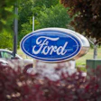 Ford logo sign mounted on pedestal surrounded by green trees and landscaping