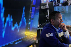 Stock trader in navy jacket monitoring financial charts on blue-lit trading floor screens