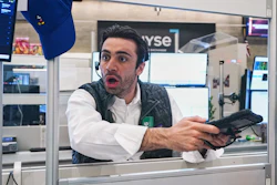 Man in white shirt and black vest holding empty wallet with surprised expression in trading floor office