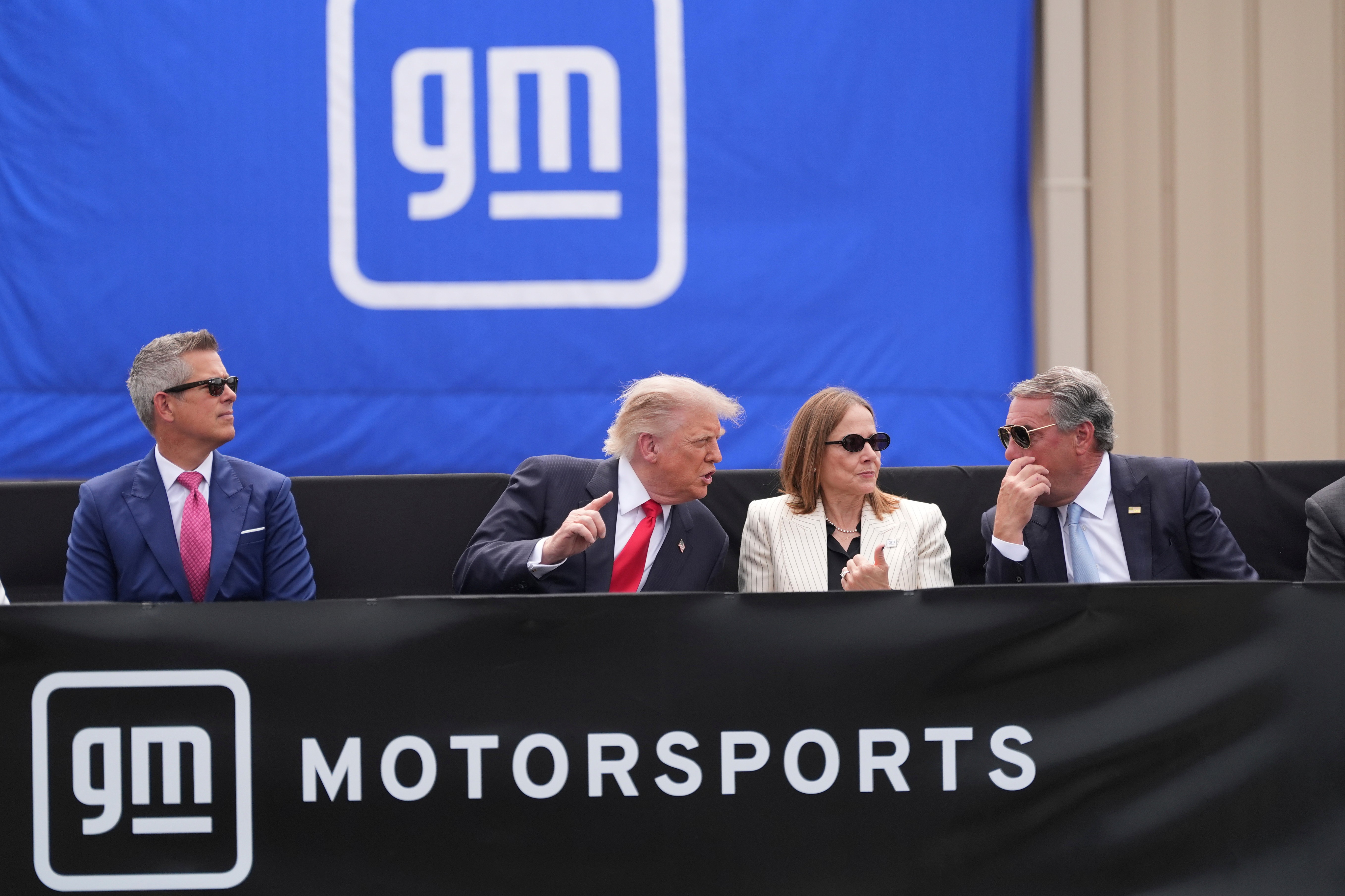 Four executives seated at a GM Motorsports branded podium during a corporate event