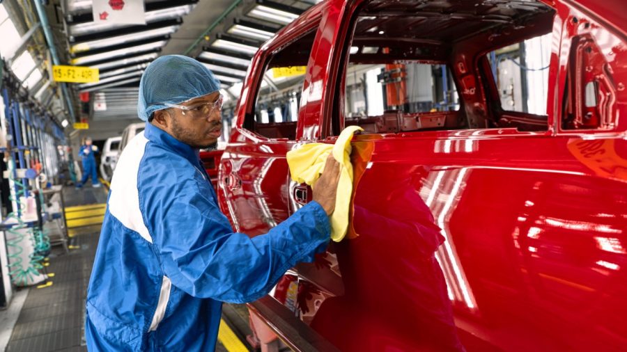 Factory worker in blue uniform polishing red vehicle body on assembly line