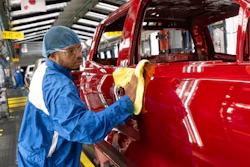 Factory worker in blue uniform polishing red vehicle body on assembly line
