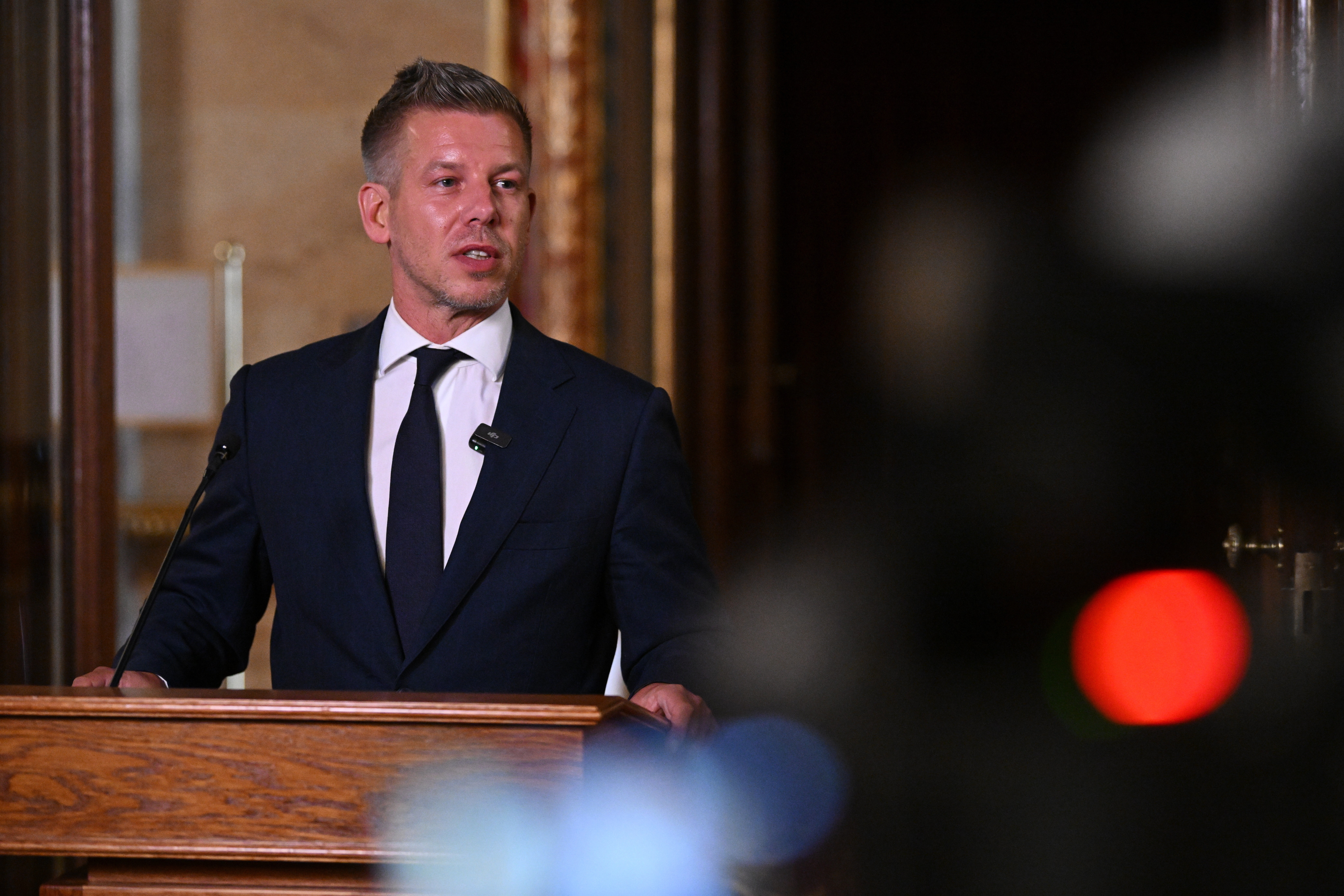 Man in dark suit and tie speaking at wooden podium during formal presentation or event