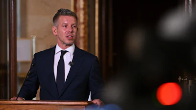 Man in dark suit and tie speaking at wooden podium during formal presentation or event