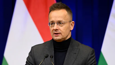 Man in glasses speaking at podium with Hungarian flag backdrop during official address