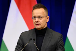 Man in glasses speaking at podium with Hungarian flag backdrop during official address