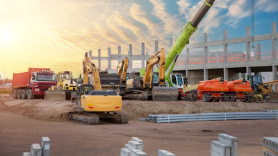 Construction site with excavators, cranes, and heavy machinery at sunset with partially built steel structure.