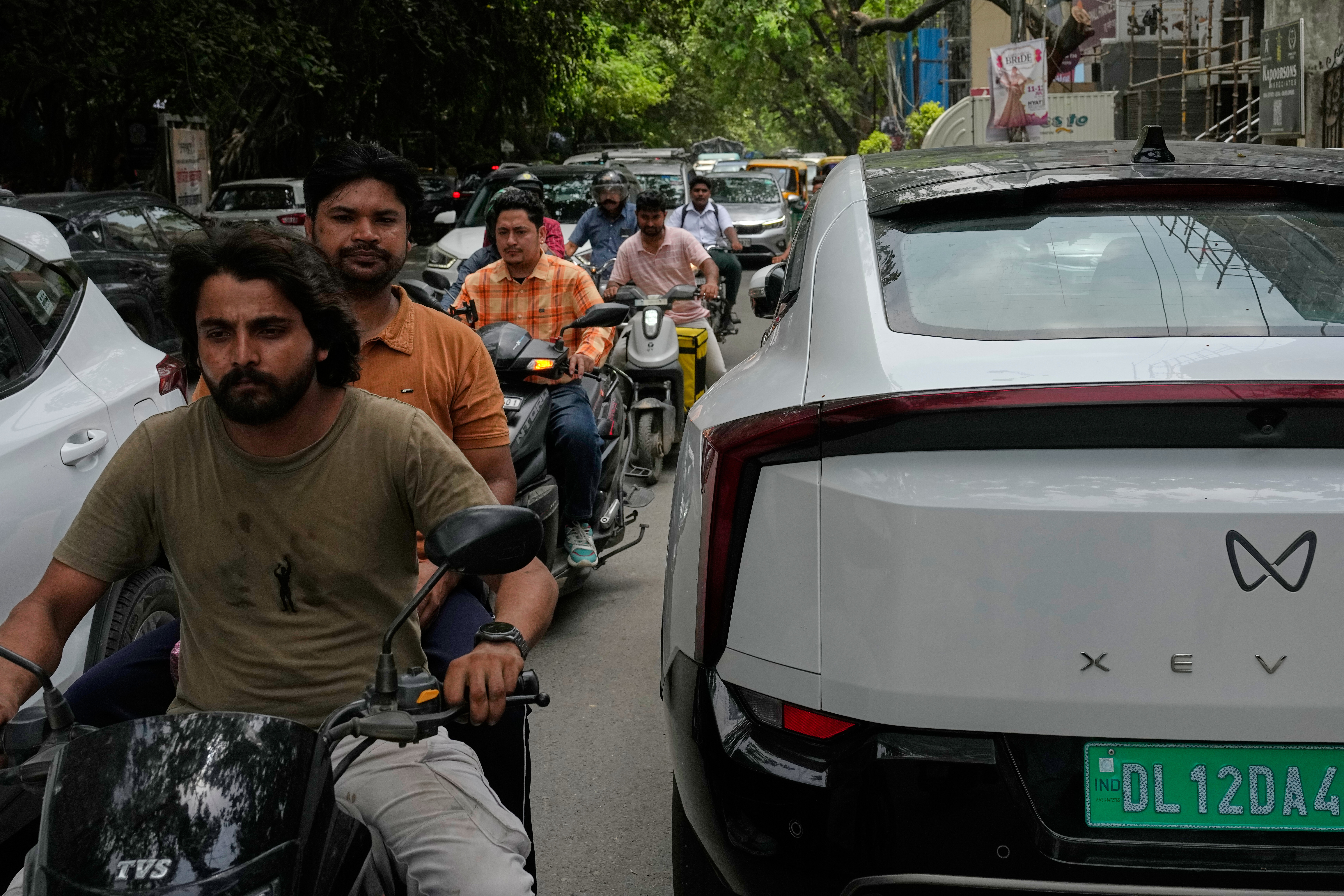 White XEV electric vehicle parked on crowded street with motorcycles and people in background