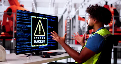 Factory worker in safety vest reacting to system hacked warning on computer monitor in industrial facility