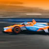 Orange and blue IndyCar racing vehicle in motion on track at sunset