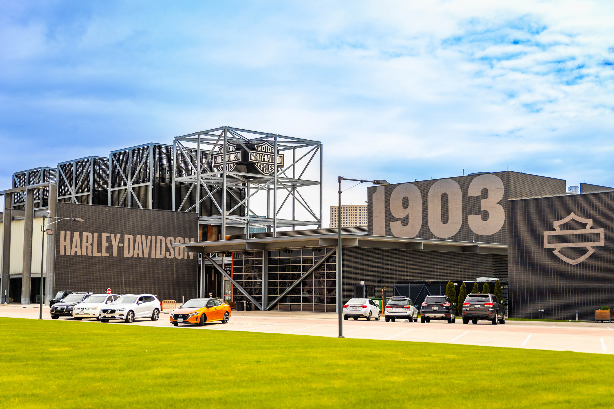 Harley-Davidson facility with 1903 establishment date, featuring industrial architecture, motorcycles parked outside, and the iconic shield logo on brown metal building.