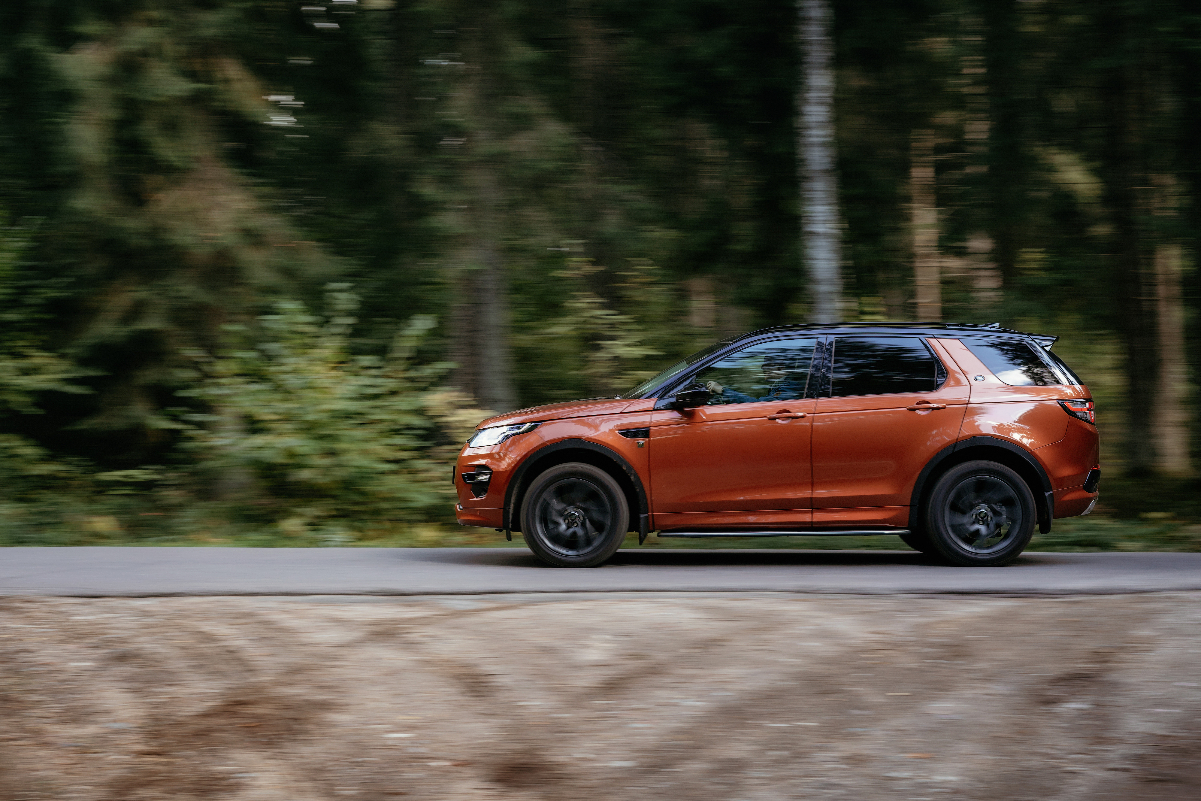 Burnt orange Land Rover Discovery Sport driving on a forest road