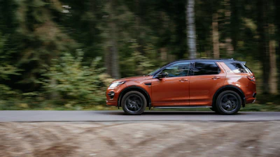 Burnt orange Land Rover Discovery Sport driving on a forest road
