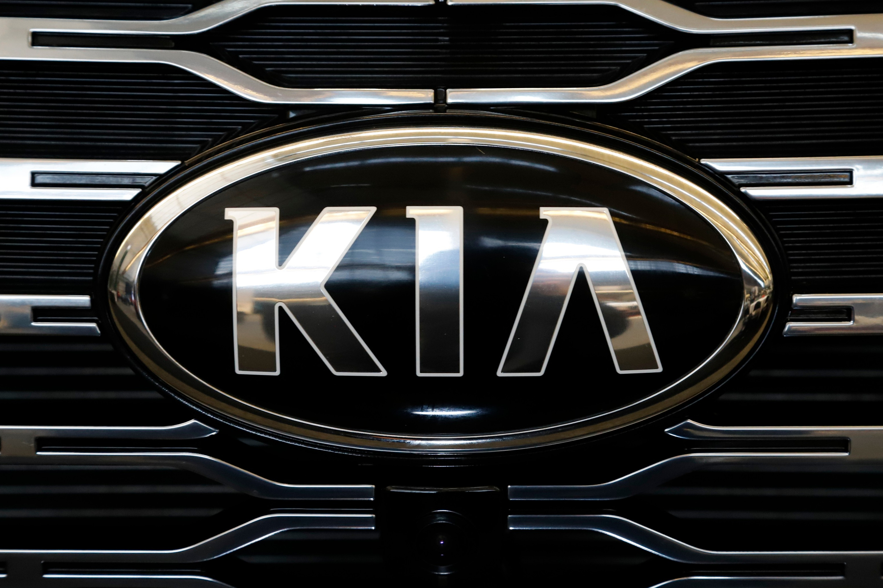 Kia logo on vehicle front grille with chrome oval frame and horizontal slat design