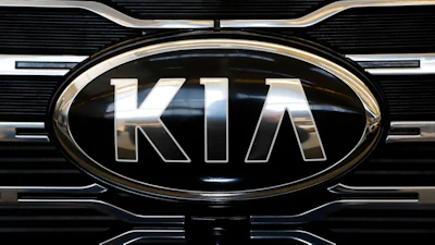 Kia logo on vehicle front grille with chrome oval frame and horizontal slat design