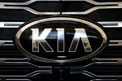 Kia logo on vehicle front grille with chrome oval frame and horizontal slat design