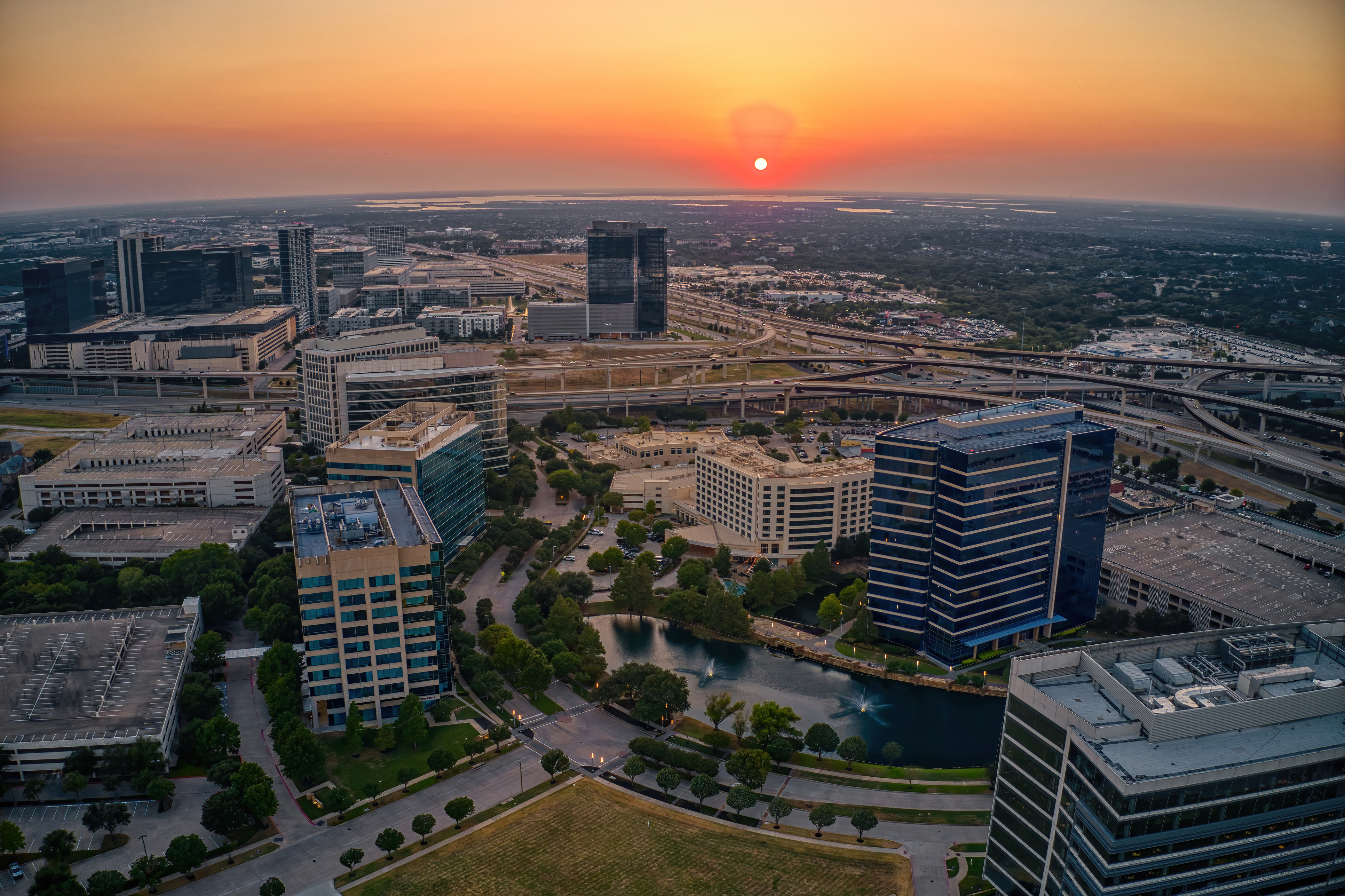 Aerial sunset view of downtown skyline with modern office buildings, highways, and waterfront development