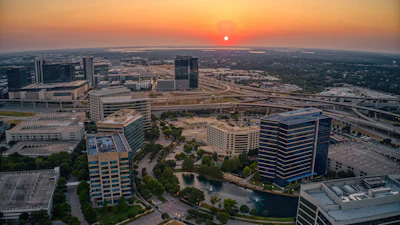Aerial sunset view of downtown skyline with modern office buildings, highways, and waterfront development
