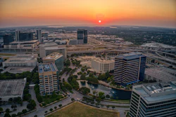 Aerial sunset view of downtown skyline with modern office buildings, highways, and waterfront development