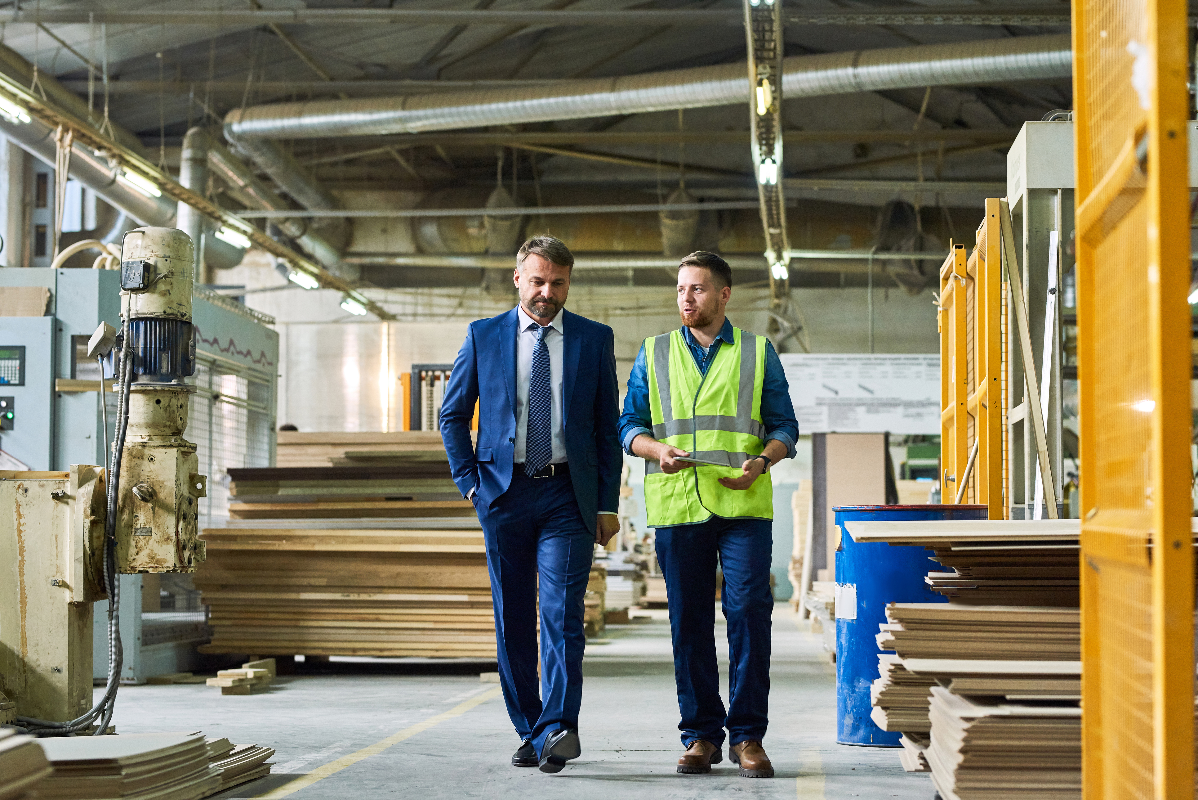 Two professionals walking through industrial manufacturing facility with machinery and yellow structural equipment