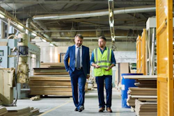 Two professionals walking through industrial manufacturing facility with machinery and yellow structural equipment
