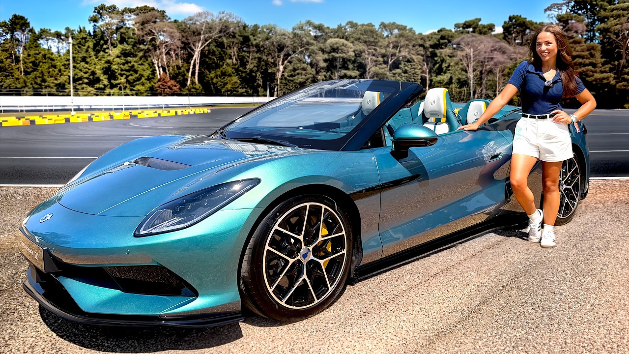Woman posing beside turquoise sports car at racing track with trees in background