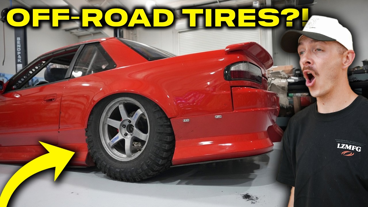 Red sports car with off-road tires in garage with surprised mechanic pointing at tire