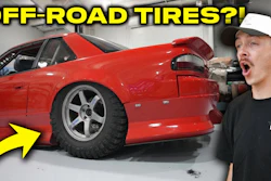 Red sports car with off-road tires in garage with surprised mechanic pointing at tire